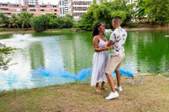 A happy Black couple celebrating their pregnancy announcement with a gender reveal blue smoke bomb.