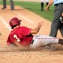 A Little League baseball player sliding into home plate with the umpire standing over them to make the call on the play.