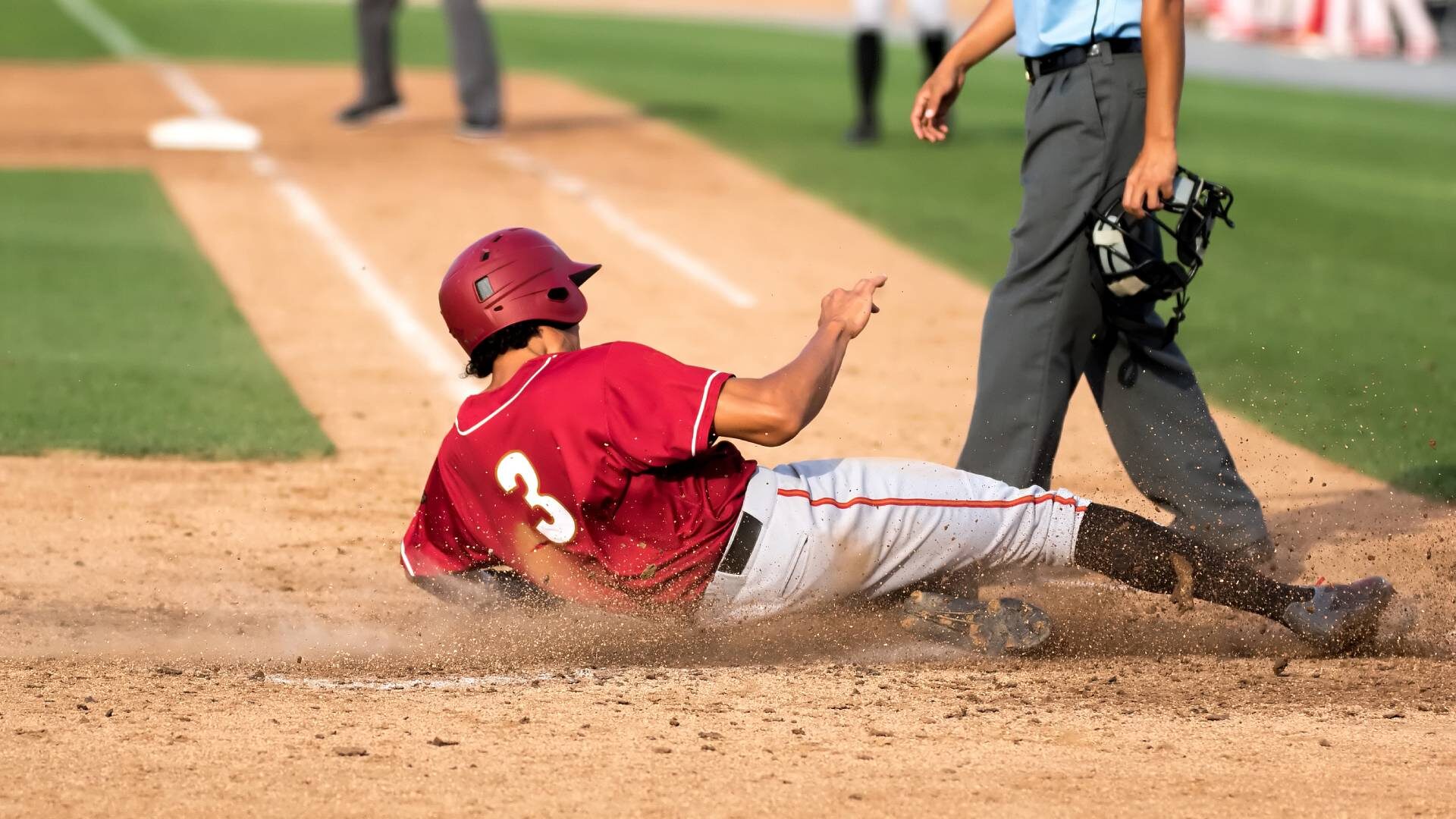 A Little League baseball player sliding into home plate with the umpire standing over them to make the call on the play.