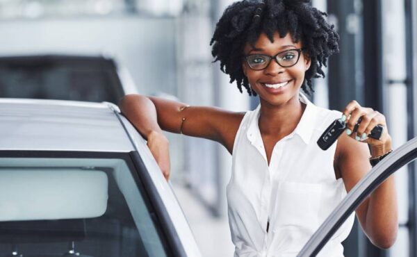 A beautiful Black woman smiling and holding up her car keys after happily making a purchase of a used car.