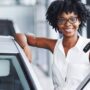 A beautiful Black woman smiling and holding up her car keys after happily making a purchase of a used car.