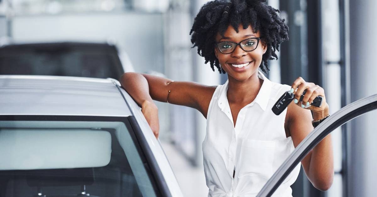 A beautiful Black woman smiling and holding up her car keys after happily making a purchase of a used car.