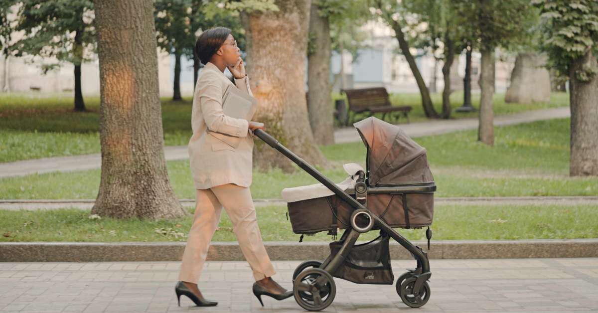 A woman wearing professional attire and high heels while pushing a stroller outside. She is talking on a cell phone.