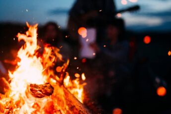 A small bonfire, crackling with red-hot flames. A family sits and stands around the fire. It's late at night.