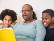 A black grandmother reads a children's book to her two black grandchildren. Her grandchildren are listening intently.