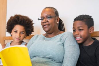 A black grandmother reads a children's book to her two black grandchildren. Her grandchildren are listening intently.