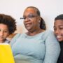 A black grandmother reads a children's book to her two black grandchildren. Her grandchildren are listening intently.