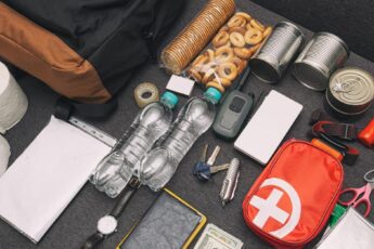 A black backpack and emergency supplies like water bottles, money, and a first aid kit on a couch.