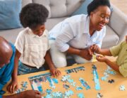 A Black family gathered around a small coffee table to complete a child-friendly skyline jigsaw puzzle together.