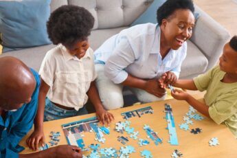 A Black family gathered around a small coffee table to complete a child-friendly skyline jigsaw puzzle together.