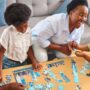 A Black family gathered around a small coffee table to complete a child-friendly skyline jigsaw puzzle together.