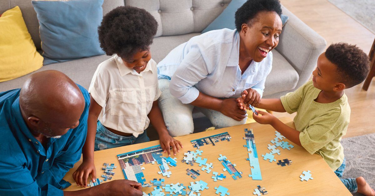 A Black family gathered around a small coffee table to complete a child-friendly skyline jigsaw puzzle together.