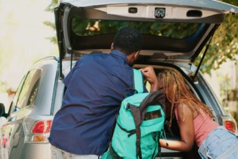 Two people loading the trunk of their car. A man is holding a teal backpack, sliding it off his shoulder.