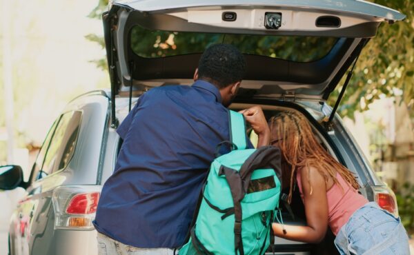 Two people loading the trunk of their car. A man is holding a teal backpack, sliding it off his shoulder.