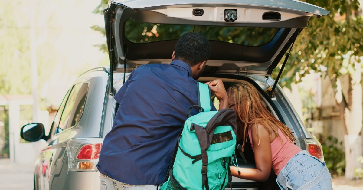 Two people loading the trunk of their car. A man is holding a teal backpack, sliding it off his shoulder.