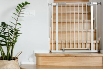 A wooden staircase with a white baby gate installed at the bottom. There is a green plant in a basket next to the stairs.