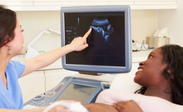 A pregnant woman lying on her back while another woman performs an ultrasound. Both are looking at the machine's screen.