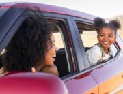 A Black mother and her young daughter in their red car. They're looking at each other from their windows.