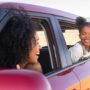 A Black mother and her young daughter in their red car. They're looking at each other from their windows.