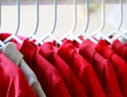 A row of red collared shirts hanging on white hangers. There is one stray gray collared shirt near the front.