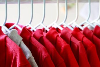 A row of red collared shirts hanging on white hangers. There is one stray gray collared shirt near the front.