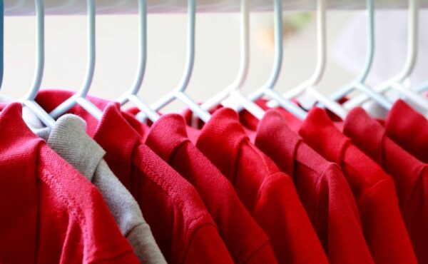 A row of red collared shirts hanging on white hangers. There is one stray gray collared shirt near the front.