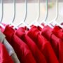 A row of red collared shirts hanging on white hangers. There is one stray gray collared shirt near the front.