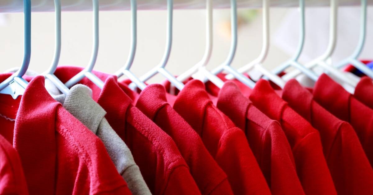 A row of red collared shirts hanging on white hangers. There is one stray gray collared shirt near the front.