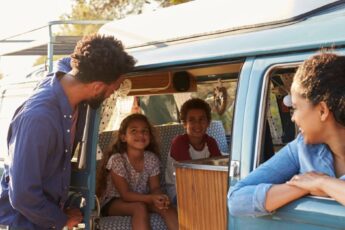 A Black family of four on an RV road trip. The mom is in the passenger seat, the kids in the back, and the dad by the door.