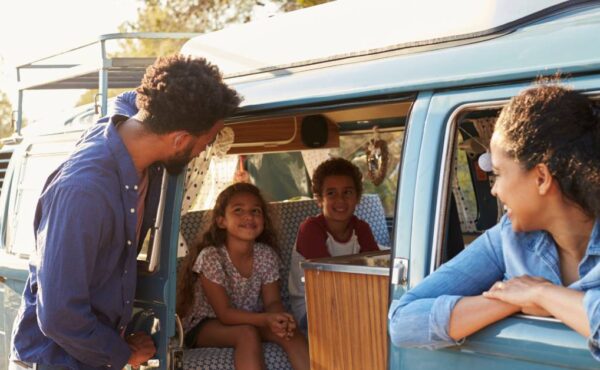 A Black family of four on an RV road trip. The mom is in the passenger seat, the kids in the back, and the dad by the door.