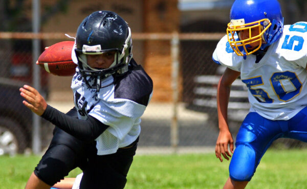 A youth football game with one athlete holding and running the ball and the opponent chasing him down for a tackle.