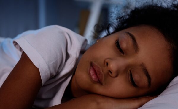 A close-up view shows a little girl with black hair sleeping on a white pillow and wearing a white t-shirt.