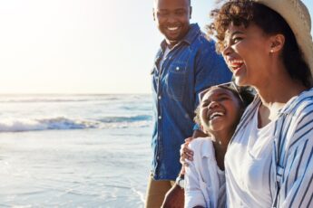 A Black family walks on a beach together. The mom, dad, and child all have smiles on their faces.