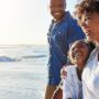 A Black family walks on a beach together. The mom, dad, and child all have smiles on their faces.