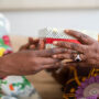 A Black adult daughter giving her grandmother a special box with a floral print. The grandmother is receiving the box.