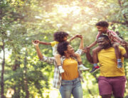 A young black family walking through the park. The parents are carrying their young children on their backs.