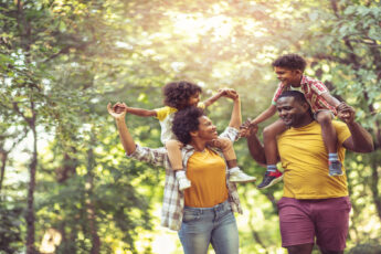 A young black family walking through the park. The parents are carrying their young children on their backs.