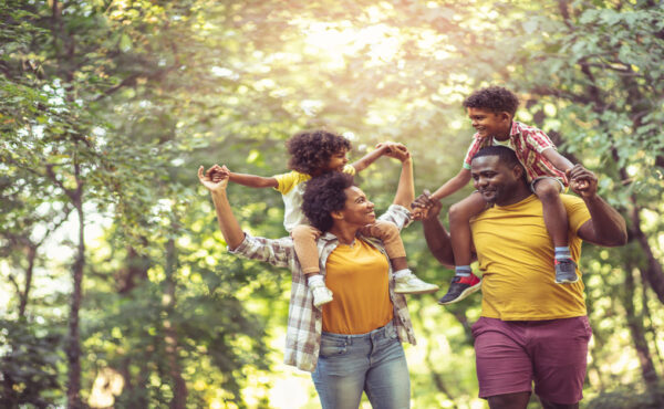 A young black family walking through the park. The parents are carrying their young children on their backs.