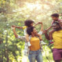 A young black family walking through the park. The parents are carrying their young children on their backs.