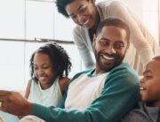 A happy Black family, a daughter, son, mom, and dad, smiles and reads together, enjoying quality time on the couch at home.