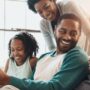 A happy Black family, a daughter, son, mom, and dad, smiles and reads together, enjoying quality time on the couch at home.