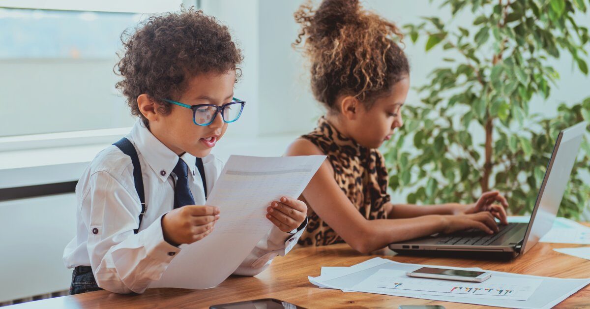 Adorable boy and girl are pretending to be professionals. The girl is typing on a laptop while the boy reads from a paper.